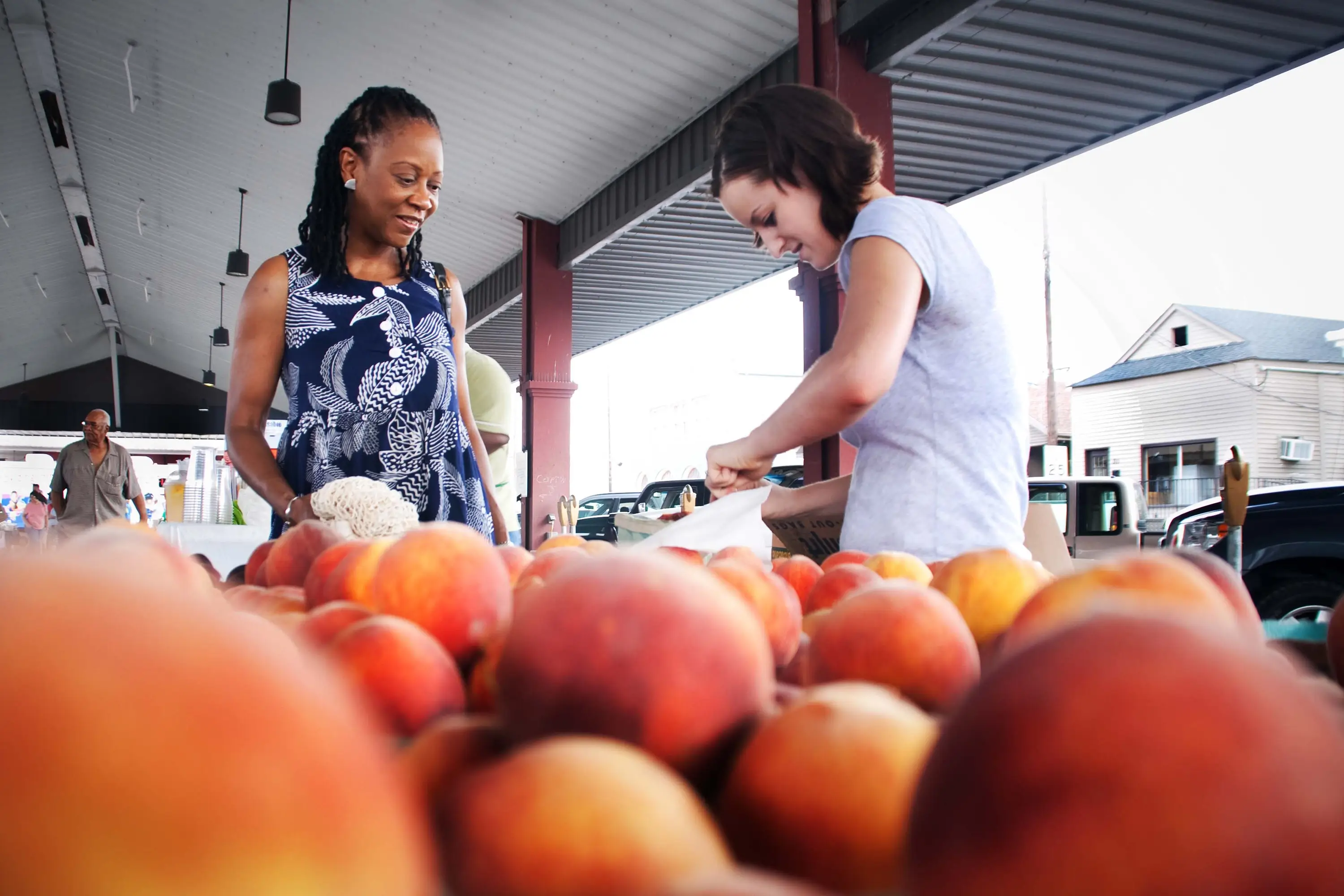 Two women at a farmer's market buying peaches