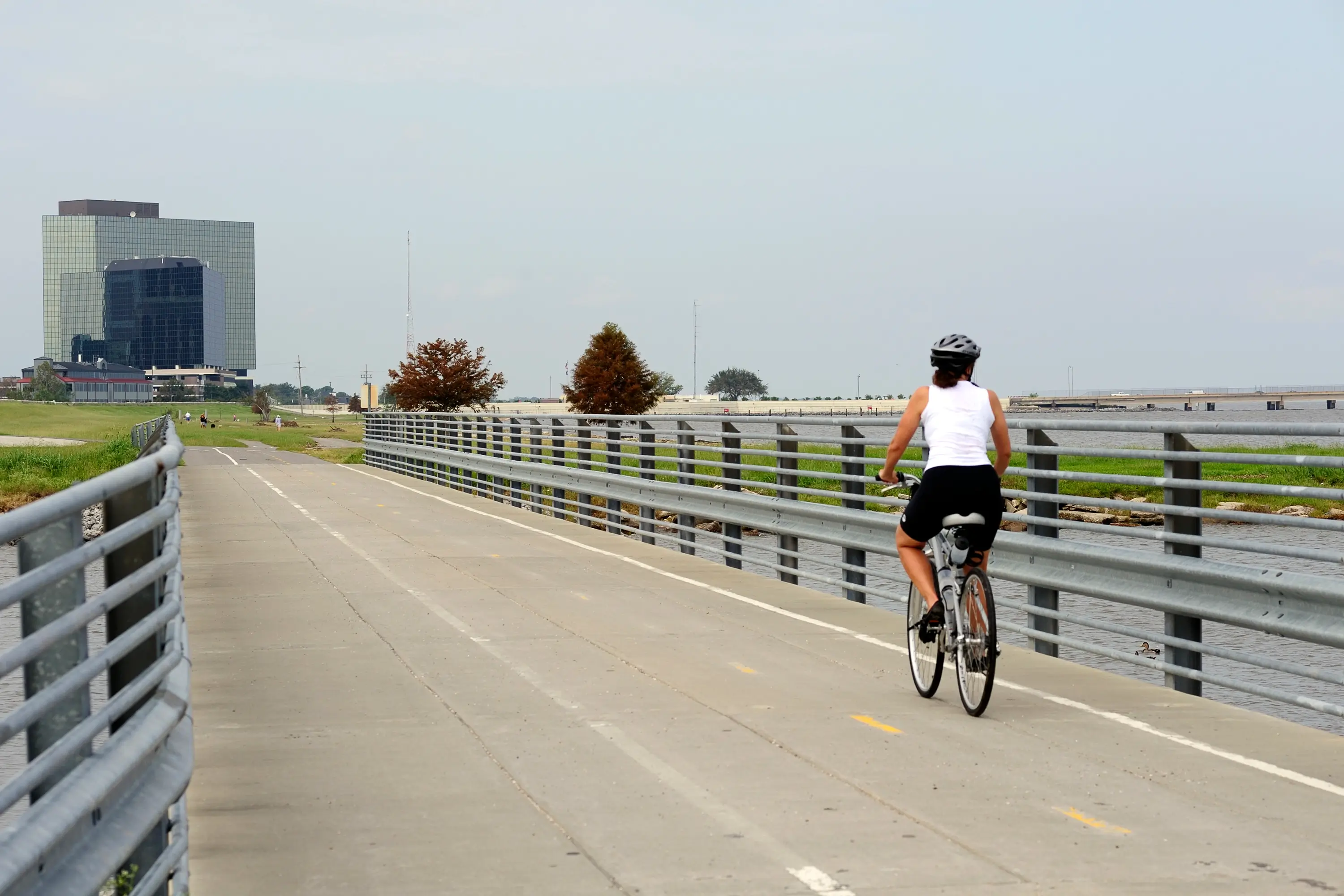 A woman riding a bike on a bridge with Metairie buildings in the background